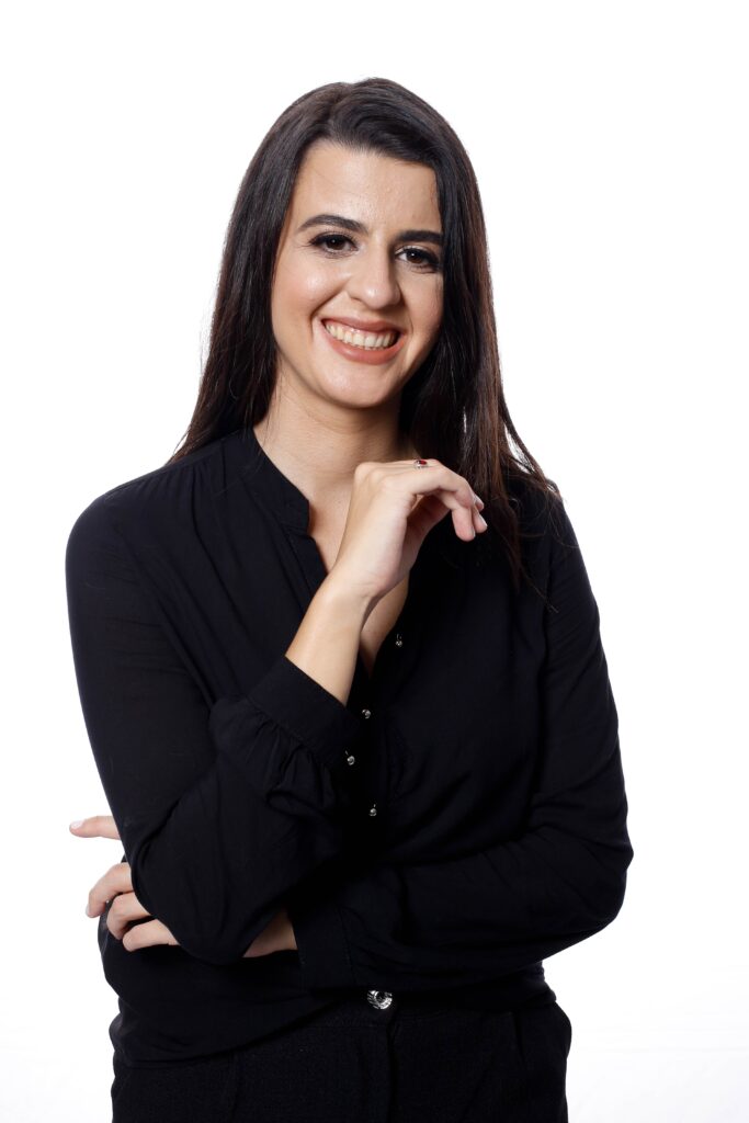 Dra Giovana Pellissari, vestida de roupa social preta, sorrindo