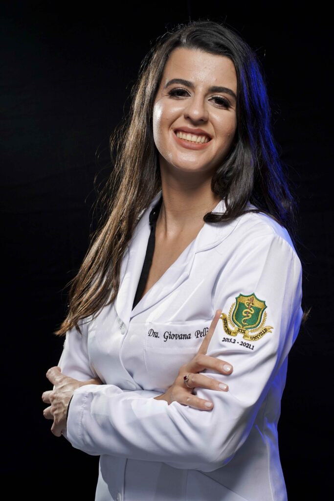 Dra Giovana Pellissari, de jaleco, braços cruzados, sorrindo.