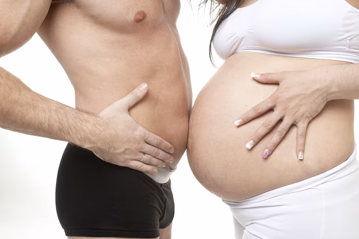 Mulher e homem, encostando as barrigas, sendo o homem magro e com barriga pequena, e a mulher com barriga de grávida, representando as diferenças entre homens e mulheres.