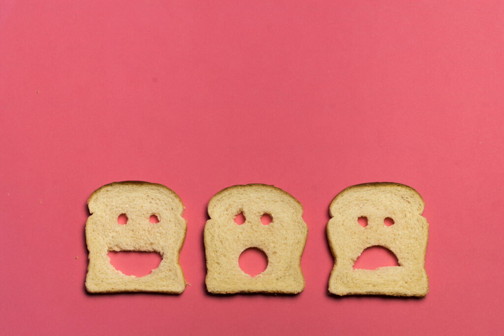 3 fatias de pão sobre um fundo rosa, com recortes representando um pãozinho sorrindo, um pãozinho assustado, e um pãozinho triste