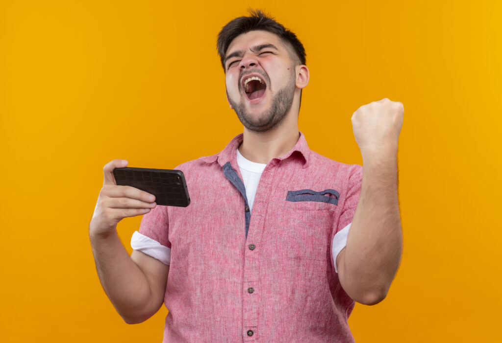 Homem com um celular na mão e expressão de muita felicidade e euforia